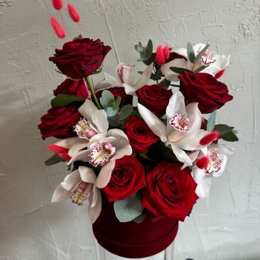 Luxurious floral arrangement featuring deep red roses and white orchids with pink accents, presented in a red velvet hatbox.