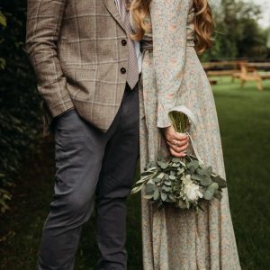 Couple standing close, with the woman holding a small white peony bouquet with eucalyptus.