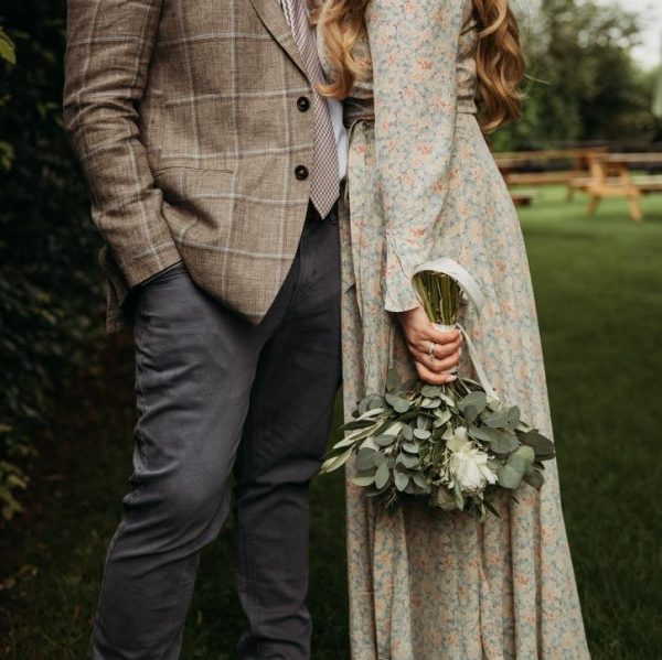 Couple standing close, with the woman holding a small white peony bouquet with eucalyptus.