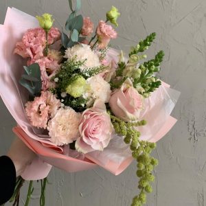 Delicate hand-tied bouquet with blush roses, carnations, lisianthus, and greenery in soft pink wrapping.