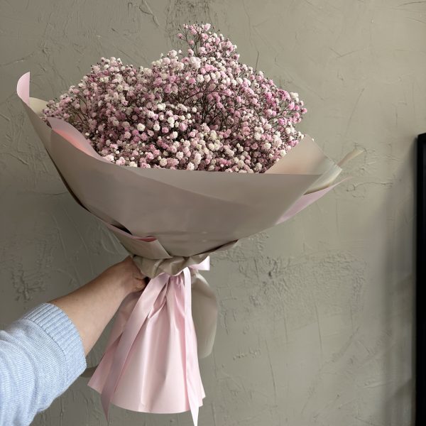 Hand holding a bouquet of delicate pink gypsophila flowers wrapped in pale pink and beige paper