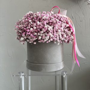 Round grey velvet box filled with pink and white gypsophila flowers, tied with pink ribbons.