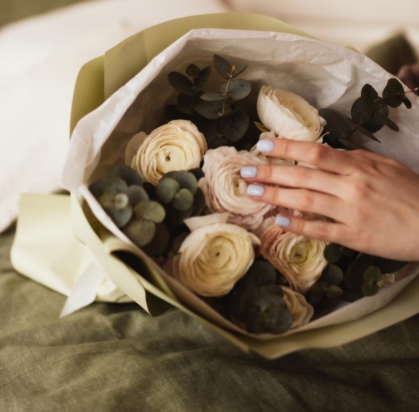 Pastel pink ranunculus bouquet with eucalyptus, elegantly wrapped in white and green paper.