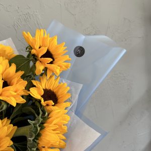 Close-up of vibrant sunflower bouquet with KS Bloomery logo on pale blue wrapping.