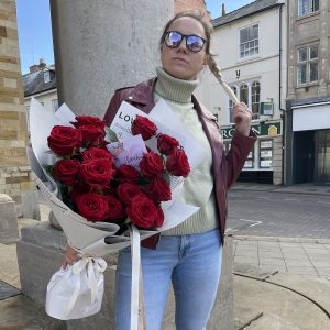 Woman holding a large bouquet of red roses wrapped in white paper with a thank-you card, standing in Northampton town centre