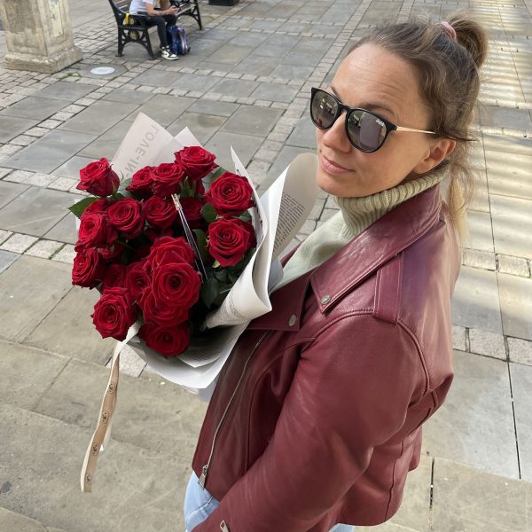 Woman in a burgundy jacket holding a bouquet of red roses wrapped in white paper on a city street