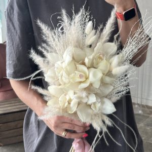 Hand-held bridal bouquet of ivory cymbidium orchids and pampas grass, captured in front of a mirror.