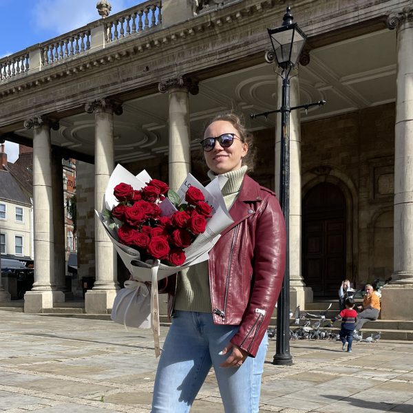 Smiling woman holding a bouquet of red roses in front of Northampton’s historic market square