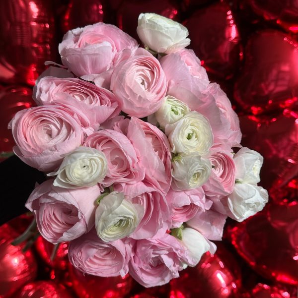 Bouquet of light pink and white ranunculus flowers against a backdrop of red heart balloons.