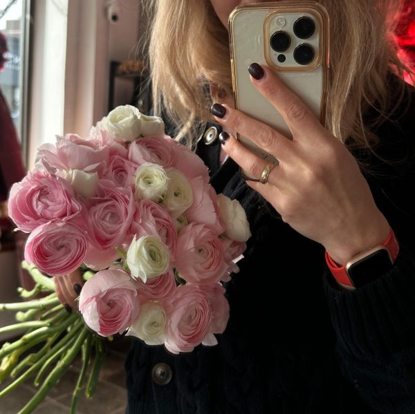 Woman holding a bouquet of soft pink and white ranunculus flowers while taking a mirror selfie.