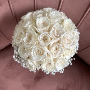 Top view of an elegant white rose and gypsophila bridal bouquet on a blush pink velvet sofa, crafted by KS Bloomery in Northampton.