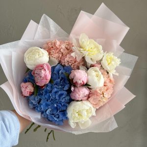 Elegant bouquet of white and pink peonies with blue and blush hydrangeas in soft pastel wrapping.