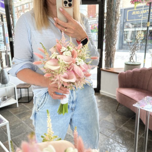 Florist holding a blush pink bridal bouquet with calla lilies and astilbe at KS Bloomery shop in Northampton.