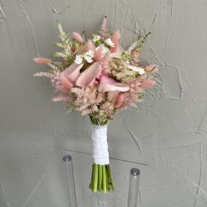 Romantic blush pink bridal bouquet with calla lilies, astilbe, and white florals, wrapped in lace ribbon.