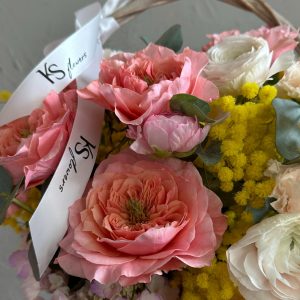 Close-up of a romantic spring bouquet with pink garden roses, white ranunculus, yellow mimosa, and KS Bloomery branded ribbon.