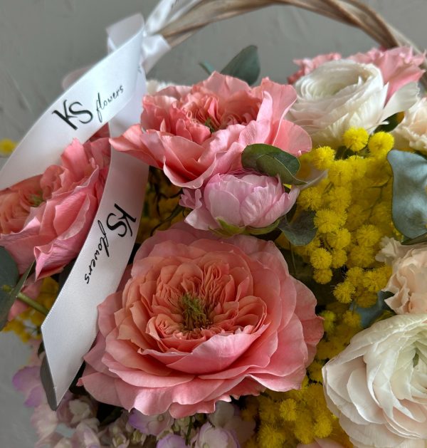 Close-up of a romantic spring bouquet with pink garden roses, white ranunculus, yellow mimosa, and KS Bloomery branded ribbon.
