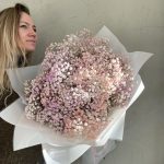 Woman holding a large pastel pink and white gypsophila bouquet wrapped in frosted white film.