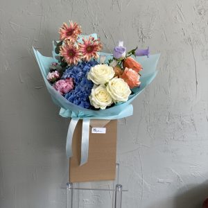 Mixed pastel bouquet with blue hydrangeas, white roses, and peach spray roses in aqua wrapping.