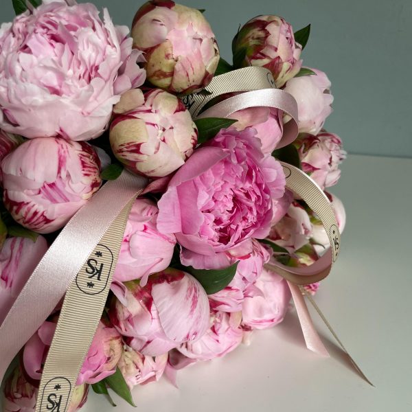 Pink peony bouquet with branded satin ribbons on white surface