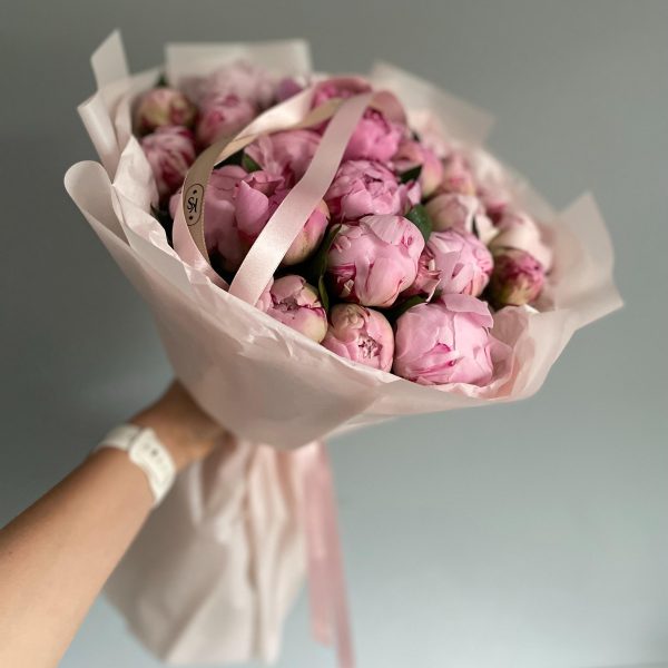 Handheld bouquet of closed pink peonies wrapped in blush paper with satin ribbon