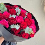 Mixed bouquet of red and hot pink roses with eucalyptus foliage in black wrapping.