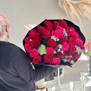 Large hand-tied bouquet of red and hot pink roses with eucalyptus, held by florist.