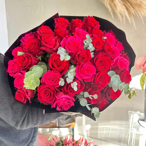Bouquet of vivid red and hot pink roses with eucalyptus, wrapped in black paper.