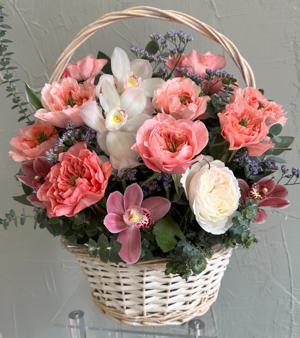 Wicker basket arrangement with coral garden roses, pink and white orchids, white rose, and eucalyptus.