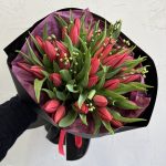 Bold red tulip bouquet with green foliage, wrapped in black and purple paper.