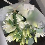 Elegant bouquet of white oriental lilies with closed and open blooms, wrapped in frosted floral paper with a KS Bloomery tag.