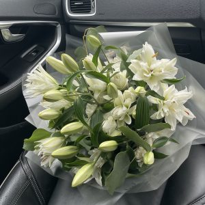Luxurious bouquet of white oriental lilies in full and bud form, resting on a car seat.