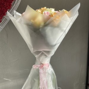 Pastel rose bouquet wrapped in elegant frosted cellophane with a soft pink ribbon, presented against a textured grey wall.