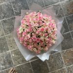 Luxurious round bouquet of pink and cream roses arranged on a tiled floor, wrapped in frosted cellophane by KS Bloomery.