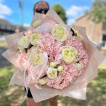 Large bouquet of soft pink hydrangeas and creamy white peonies held outdoors on a sunny day.