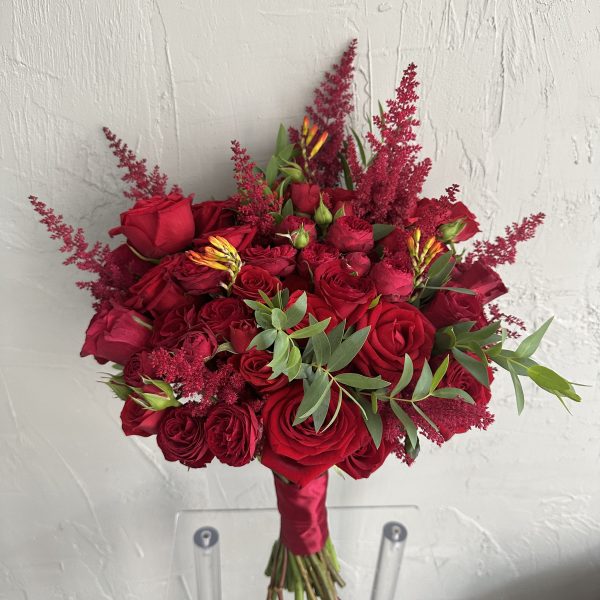 Bridal bouquet of deep red roses, astilbe, and greenery wrapped in red satin ribbon.