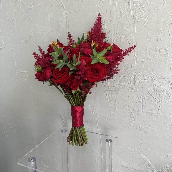 Elegant bridal bouquet with red roses, burgundy astilbe, and green foliage tied with red satin ribbon.