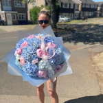 Bouquet of pastel blue hydrangeas and pink peonies held by a woman outdoors on a sunny day.
