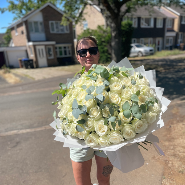 Woman outdoors in Northampton holding a large bouquet of white roses and eucalyptus.