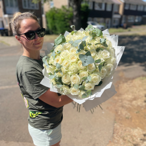 Smiling woman holding a large bouquet of white roses with eucalyptus in a residential street in Northampton.