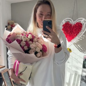 Woman holding a bouquet of blush and fuchsia roses in pink wrapping, standing in a well-lit floral boutique.