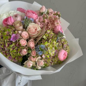 Elegant bouquet of pink roses, ranunculus and green hydrangeas wrapped in white paper.