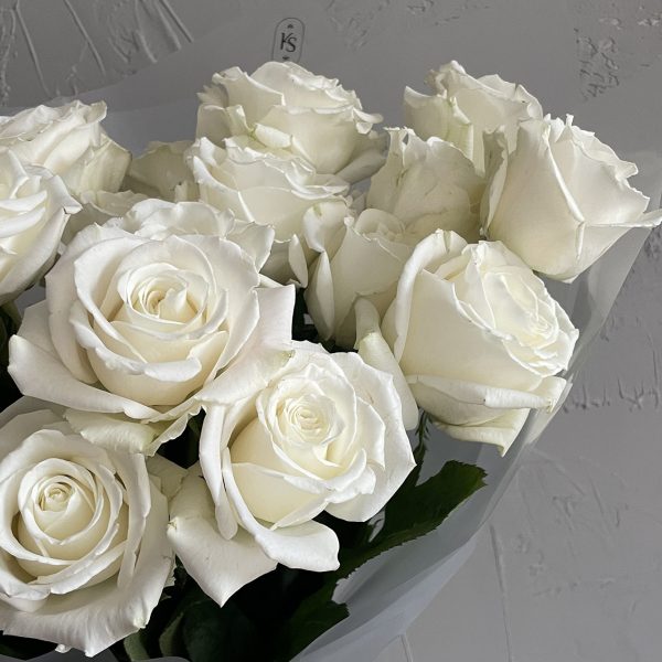 Close-up of elegant white rose bouquet wrapped in translucent paper with KS Bloomery branding.