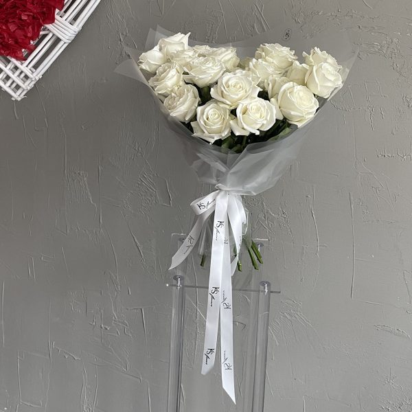 White rose bouquet tied with KS Bloomery ribbon, displayed against a textured grey wall.