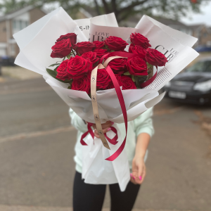 Large bouquet of red roses held in front of face, wrapped in white paper with red ribbon by KS Bloomery