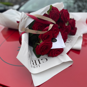 Romantic bouquet of deep red roses wrapped in white paper with ribbon, resting on a red car bonnet