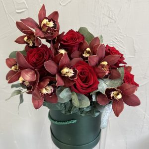 Close-up of red roses and burgundy orchids in an emerald green hat box.