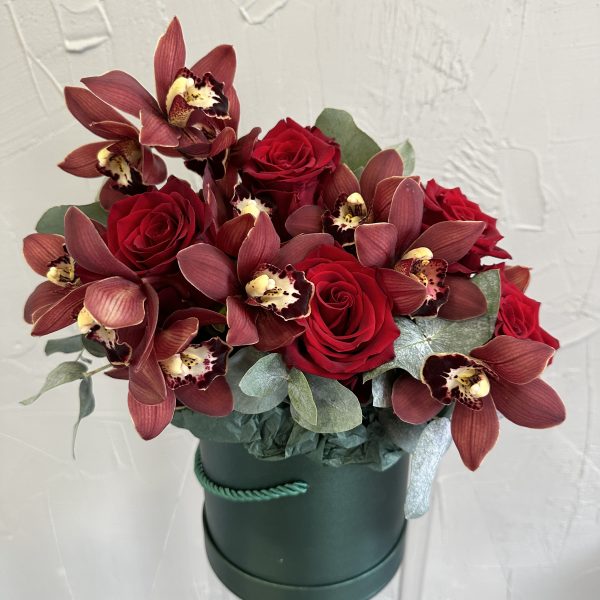 Close-up of red roses and burgundy orchids in an emerald green hat box.