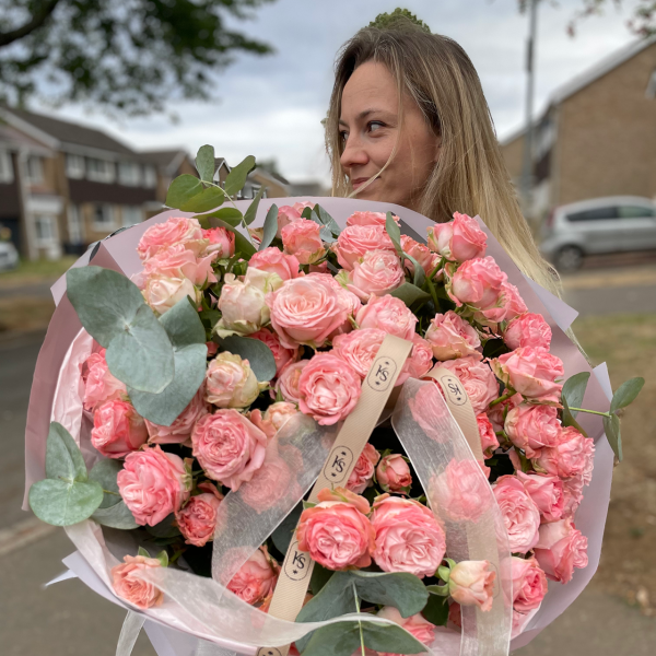 Woman holding a luxurious bouquet of soft pink spray roses with eucalyptus, tied with KS Bloomery branded ribbons.