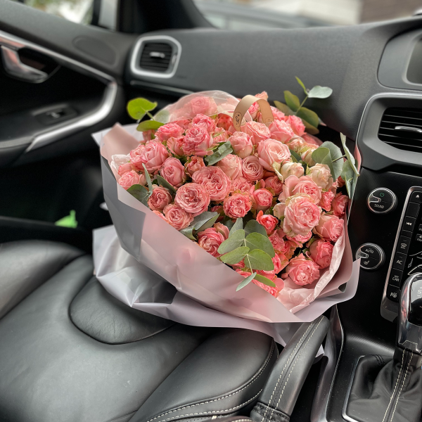 Elegant bouquet of pink spray roses with eucalyptus leaves, resting on the front seat of a car.