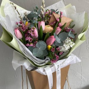 Spring bouquet in kraft gift bag with pink tulips, ranunculus, waxflowers, eucalyptus, and pussy willow, decorated with white KS Bloomery ribbon.